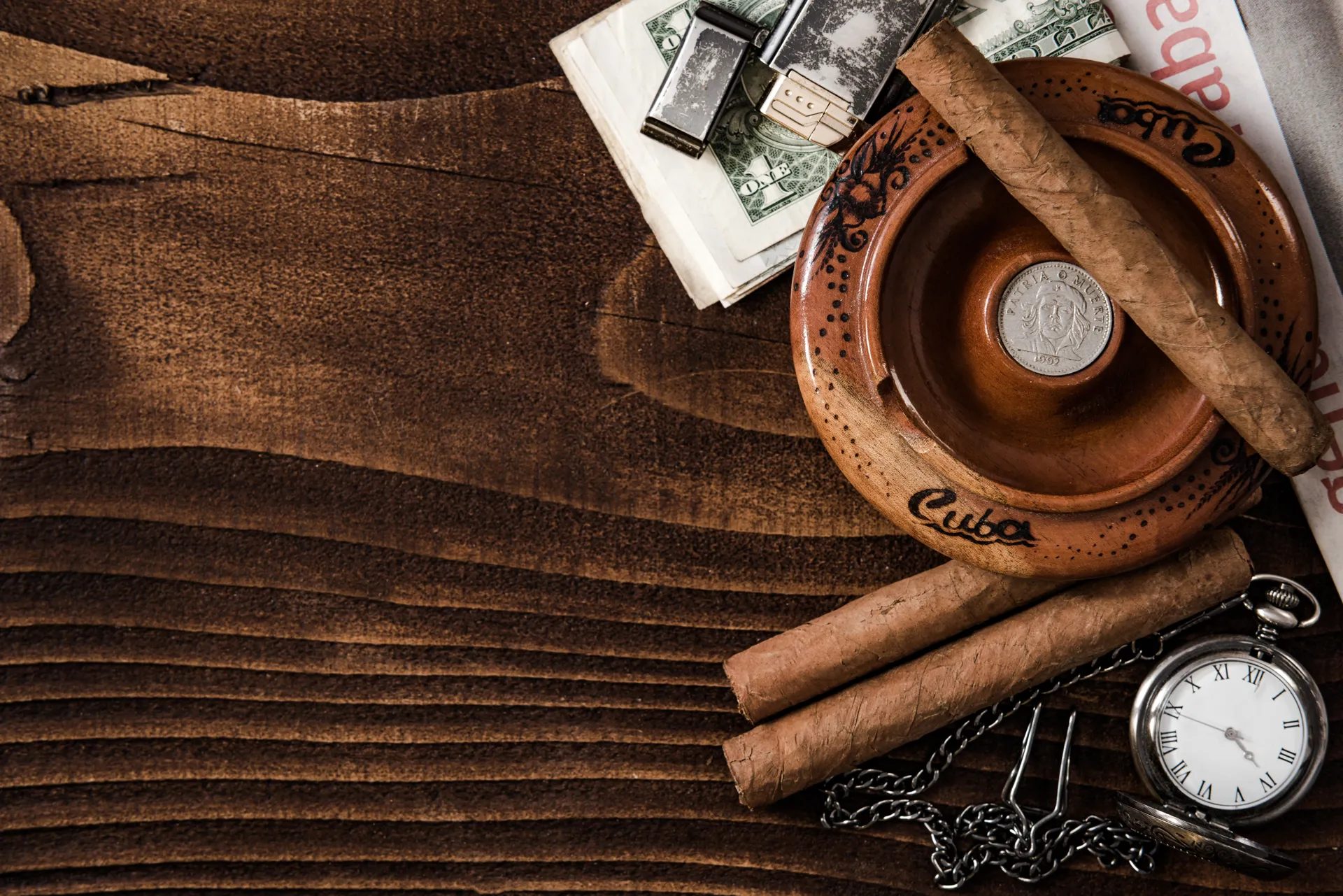 Cigarrillos cubanos sobre una mesa de madera, acompañados de un cenicero de barro, un reloj de bolsillo y billetes, creando una atmósfera sofisticada.